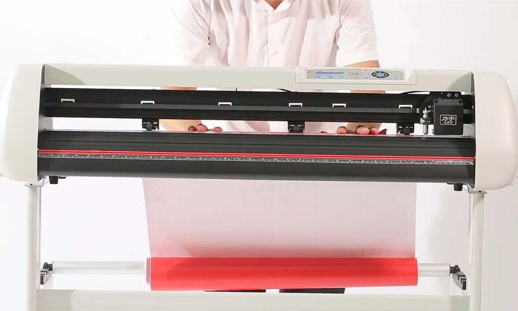 Seorang Teknisi Sedang Menyesuaikan Bahan Sticker Berwarna Merah Pada Mesin Cutting.