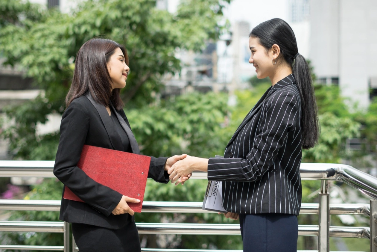 Dua Profesional Wanita Berjabat Tangan, Melambangkan Kemitraan Bisnis Yang Sukses.
