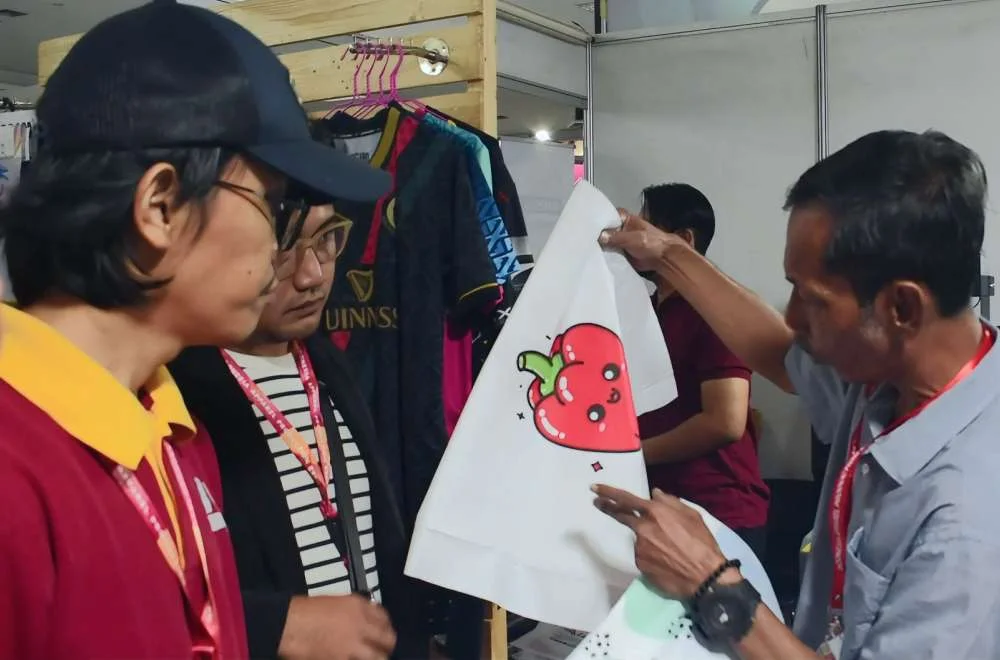 Pengunjung Melihat Contoh Hasil Cetak Kaos Saat Konsultasi Di Booth Kenduri Sablon Jogja 2026.