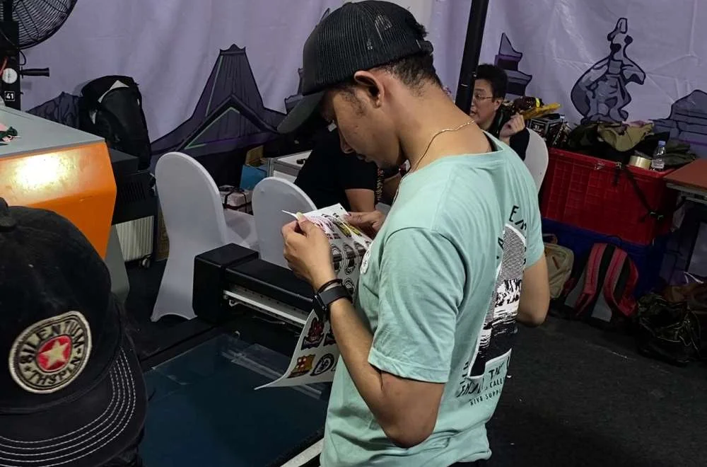 Pengunjung Mengamati Hasil Cetak Dan Proses Produksi Digital Printing Di Area Pameran Kenduri Sablon Jogja #3 Untuk Mencari Inspirasi Dan Peluang Bisnis.