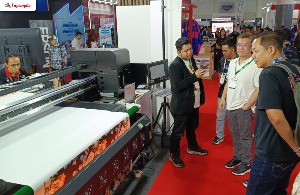 Pengunjung Melihat Demonstrasi Mesin Printing Laysander Di Area Pameran Sebagai Solusi Untuk Meningkatkan Produksi Garmen Dan Tekstil.