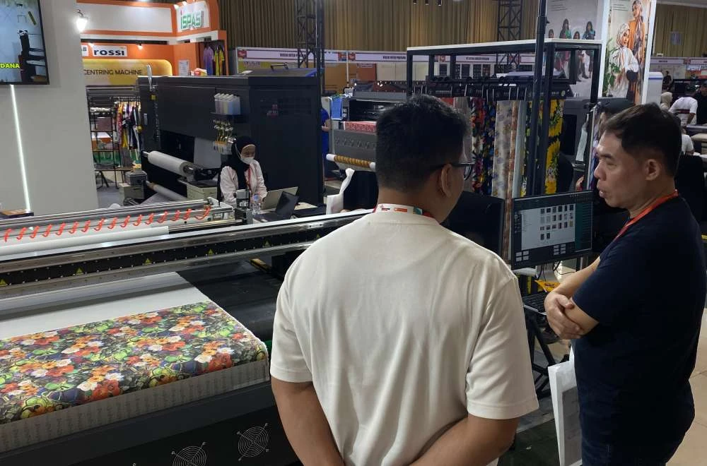 Pengunjung Melihat Proses Test Print Mesin Tekstil Laysander Di Iape Bandung 2026 Dengan Hasil Cetak Motif Bunga.
